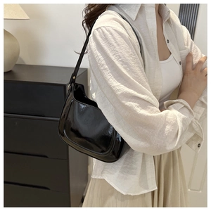 Chic black patent leather underarm bag with glossy finish shown on model's shoulder
