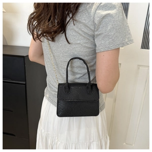 Détail du sac à main noir à texture litchi avec chaîne dorée élégante et poignée