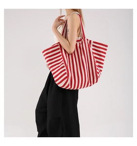 Close-up of a large red and white striped canvas tote bag worn by a fashion model