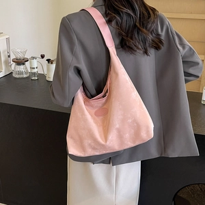 Grand sac hobo rose en daim doux porté par un mannequin dans un café au style moderne