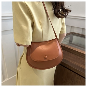Elegant caramel saddle bag paired with a yellow dress shown in a minimalist interior