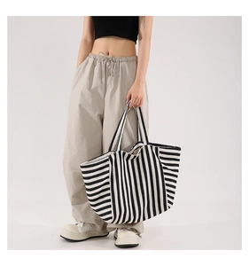 Detail of a large black and white striped tote bag held by a model in a studio
