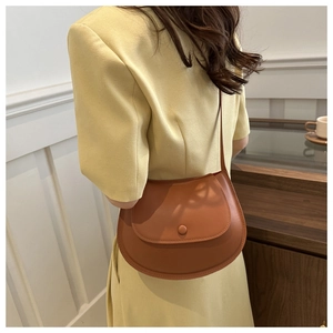 Caramel saddle bag with a round buckle worn over a beige blazer in a warm cafe setting
