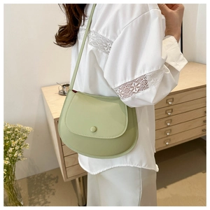 Close-up of stylish light green saddle bag with chain strap worn by a model in soft light