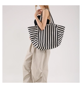 Detailed view of the black and white striped canvas tote bag worn by a model in studio