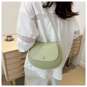Detail of light green leather saddle bag featuring a circular buckle and crossbody strap