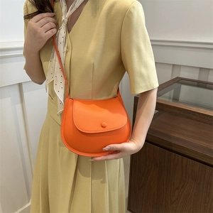 Chic orange leather saddle bag with flap closure shown on model in stylish interior setting