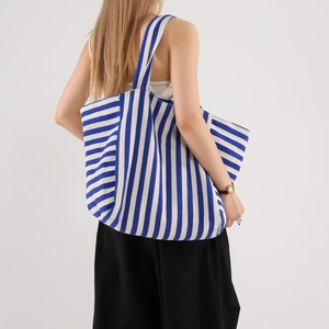 Minimalist blue and white striped canvas tote bag shown on model in a modern interior
