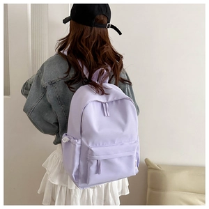Detail view of a lavender purple nylon backpack with front zipper pocket on model