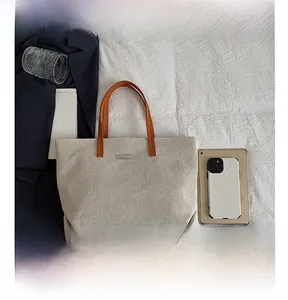 Detailed top view of large beige canvas tote bag with brown handles and a metal plate