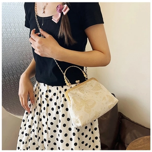Dettaglio borsa a conchiglia beige vintage con ricamo farfalla dorata e catenina