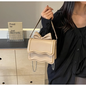 Detail of beige crossbody bag with large bow decoration and wavy edge flap design