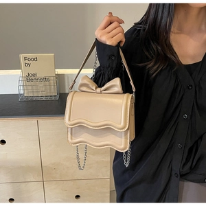 Detail of beige crossbody bag featuring bow decoration and scalloped flap edge