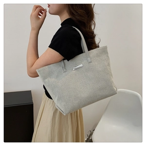 Detail of light gray canvas tote bag with silver metal patch and minimalist design