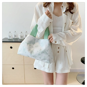 Détail d'un sac cabas en toile blanche avec motifs papillons verts et anses en tissu