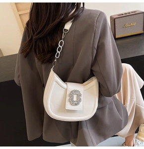 Close-up of white crescent bag with rhinestone buckle and chain strap on female model