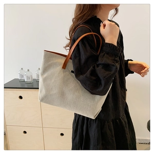 Detail of cream canvas tote bag with brown leather handles worn over the shoulder