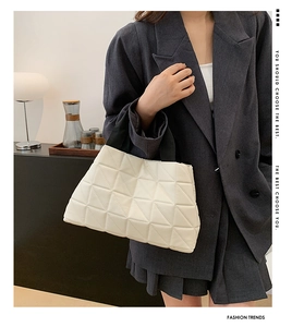 Quilted beige tote bag detail showing geometric texture and black handles on a gray suit