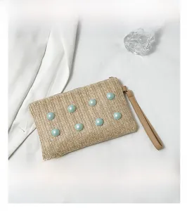 Detail of woven straw handbag featuring light blue pearls and smooth faux leather wrist strap