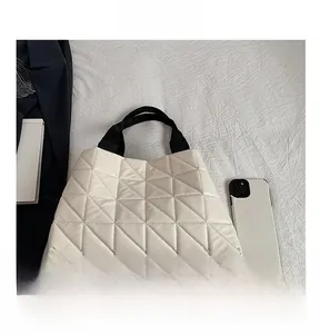 Quilted off-white tote bag with geometric stitching and black handles next to a smartphone