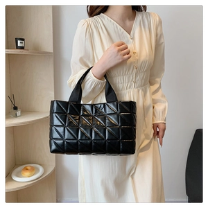 Detail of black tote bag featuring large triangular quilted patterns and durable webbing straps