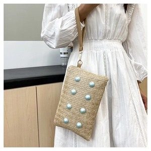 Detailed view of woven straw clutch bag with light blue resin pearl accents and leather strap
