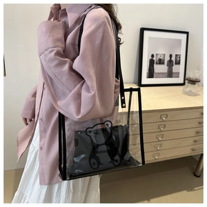 Detailed view of clear PVC tote bag with black bear pouch worn by a model in a room