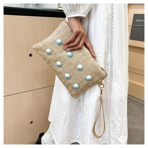 Close-up of woven beige straw clutch bag with blue pearl beads and leather wristlet