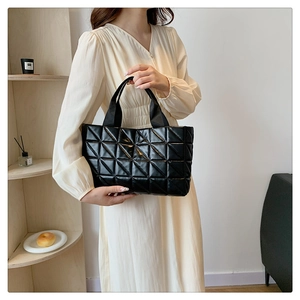 Detail of black quilted tote bag with triangle stitching on shiny PU leather surface