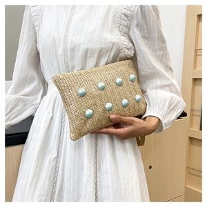 Detail of hand-woven straw clutch bag featuring decorative light blue buttons and V-texture