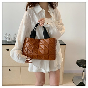 Detail of a brown quilted tote bag featuring geometric patterns and sturdy black handles