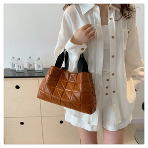Detail of deep brown quilted tote bag featuring geometric triangular patterns and black strap