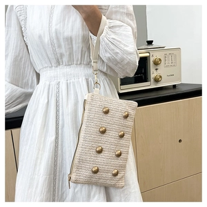 Detail of woven straw clutch with gold studs and PU wristlet strap in a summer setting
