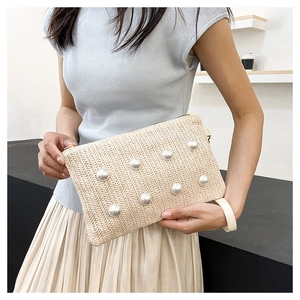 Detail of woven straw handbag featuring large faux pearl accents and leather wristlet strap
