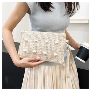 Detail shot of beige woven hand clutch with large pearl beads and wrist strap