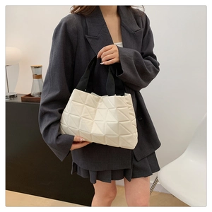 Minimalist beige tote bag with triangle quilting and black handles worn by a model