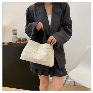 Detail of white quilted tote bag featuring geometric patterns and black woven handles