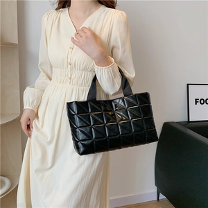 Chic black quilted tote bag with lattice pattern held by model in casual dress