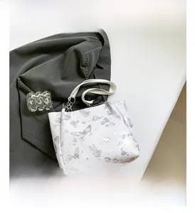 Detail van witte tote bag met vlinderprint en zilverkleurige metalen kettinggrepen