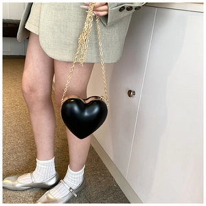 Dettaglio della borsa a catena nera a cuore indossata con un completo verde moderno