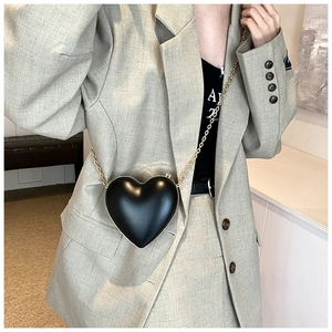 Close-up of heart-shaped crossbody bag in matte black with gold chain strap on model