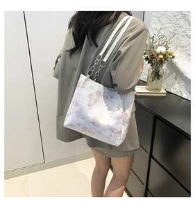 Schouderaanzicht van witte tote bag met vlinderprints en zilveren metalen ringen