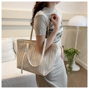Detail of a beige woven straw tote bag with white leather straps shown on a shoulder