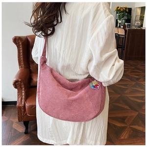 Detail showing pink corduroy crescent crossbody bag with a colorful bear charm