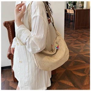 Detail of beige corduroy crescent shoulder bag with a colorful cartoon bear charm