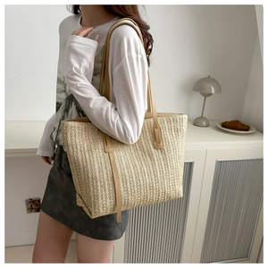Detailed view of large straw tote bag with brown handles worn on shoulder for summer