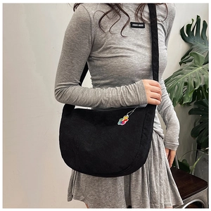 Detail of black corduroy crescent crossbody bag with cute bear charm on shoulder strap