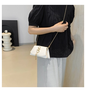 Close-up of white leather crossbody bag with gold metal logo and chain strap on model