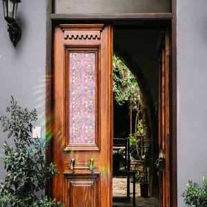 Floral stained glass film on vintage wooden door with prismatic sunlight effect
