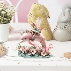 Close-up of a 2D flat acrylic fairy and pink dolphin ornament in a cozy home setting